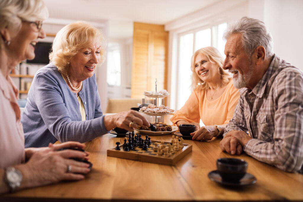 Group of mature friends enjoying while playing chess during coffee time at home.